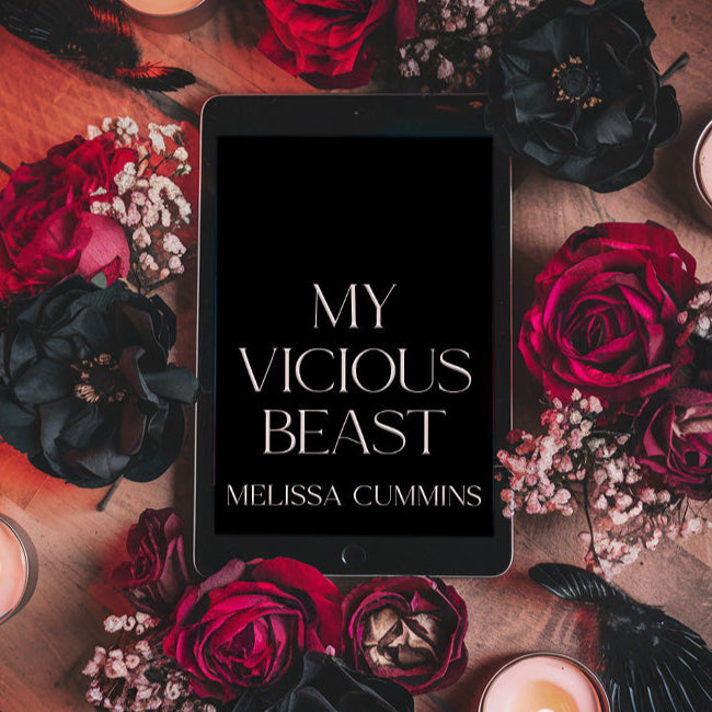 Tablet displaying 'My Vicious Beast' by Melissa Cummins surrounded by red and black roses and candles on a wooden surface.